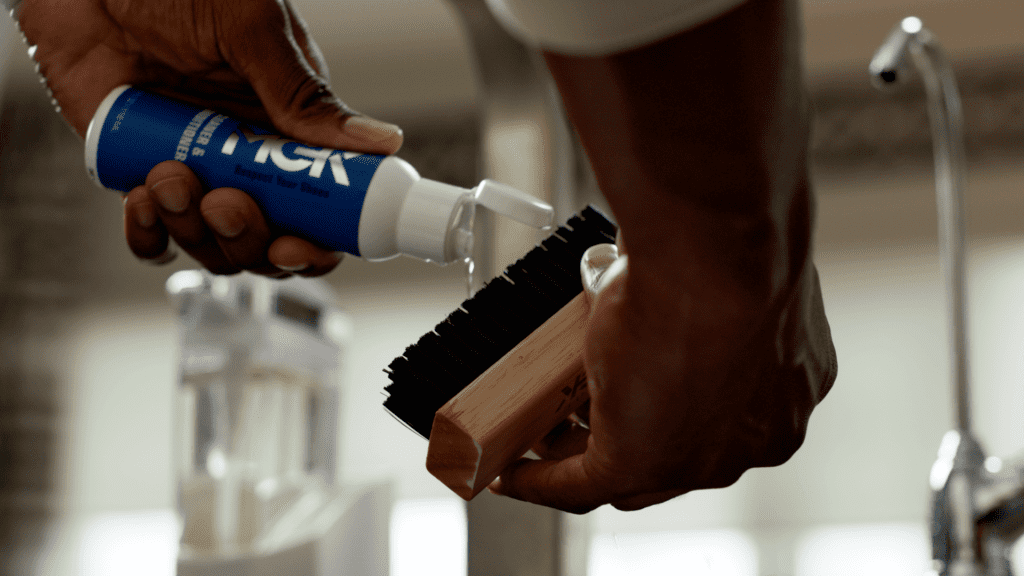 Man pours Shoe MGK Cleaner and Conditioner onto a nylon shoe brush