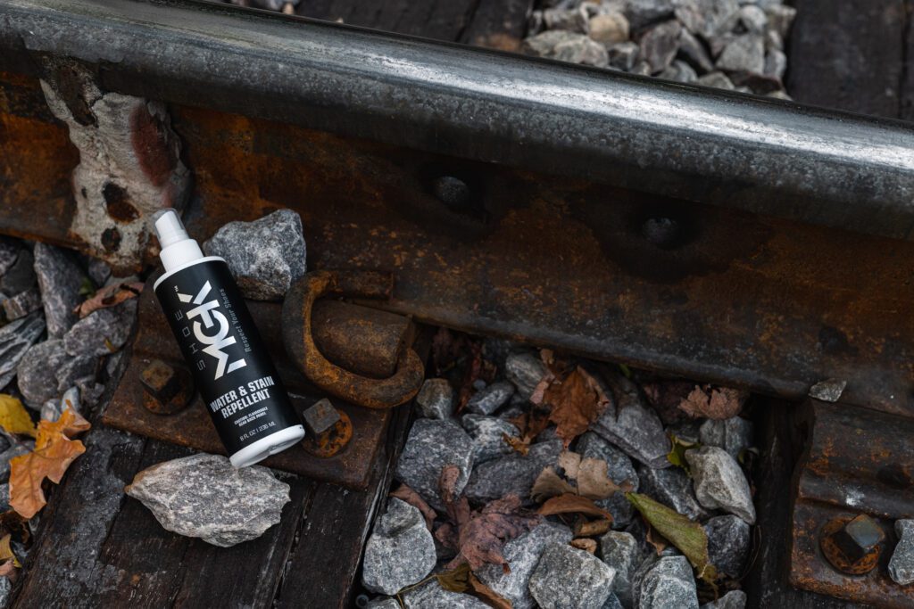 A bottle of the Shoe MGK Water and Stain Repellent on a train track