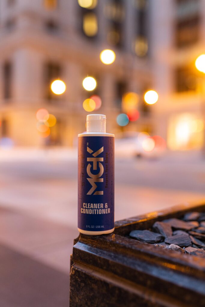 A bottle of the Shoe MGK Cleaner and Conditioner lit by city lights