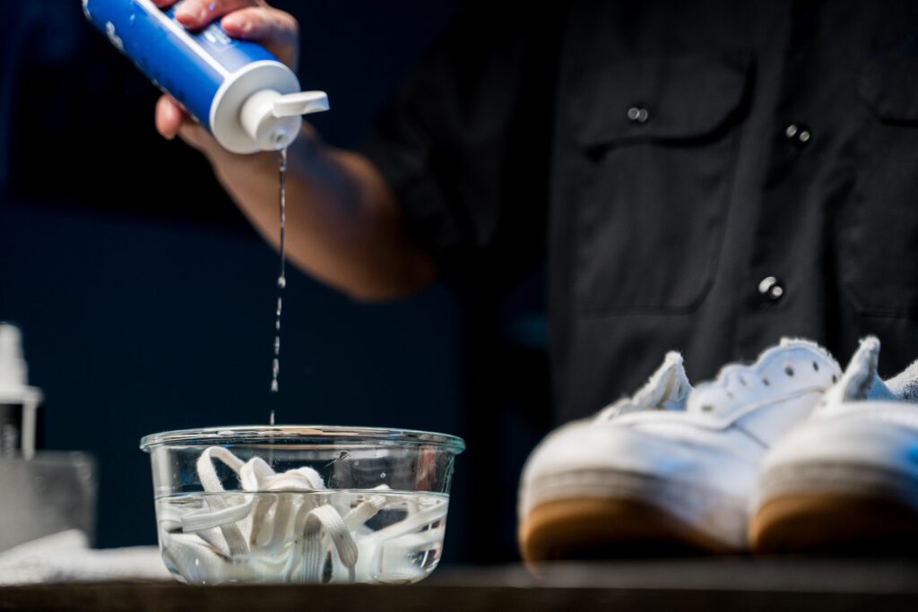 Man pours the Shoe MGK Cleaner and Conditioner into a bowl of water with shoe laces inside