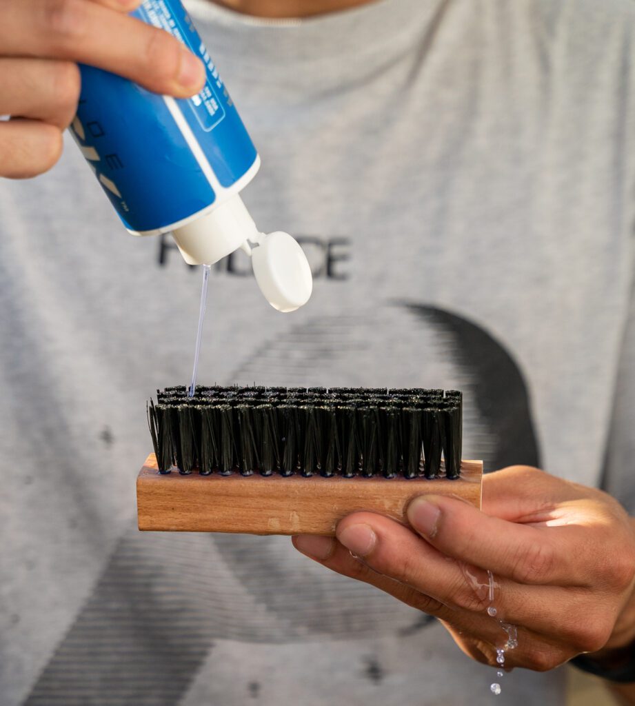 Man pours the Shoe MGK Cleaner and Conditioner onto a nylon shoe brush