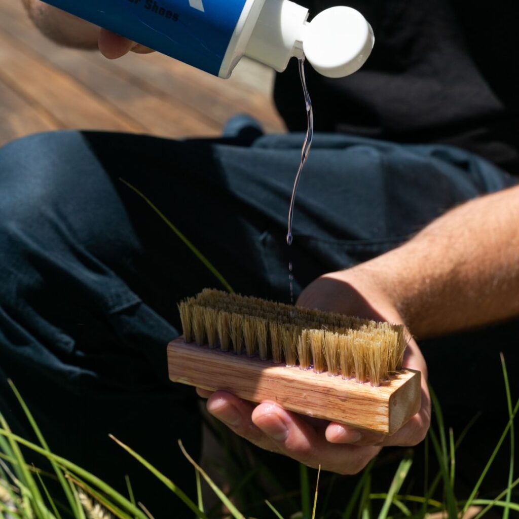 Man pours the Shoe MGK Cleaner and Conditioner onto a shoe brush