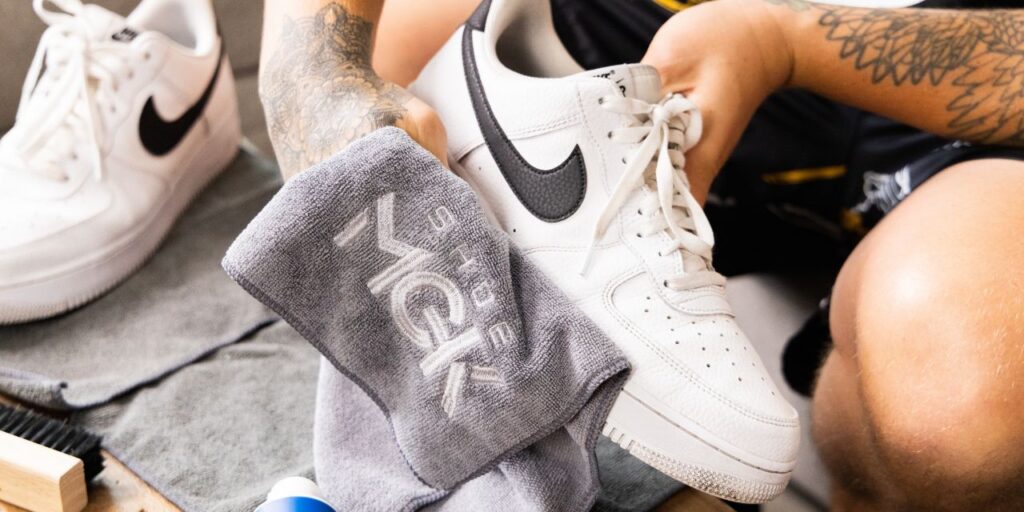 Man dries off white Nike shoes with a microfiber towel that reads Shoe MGK