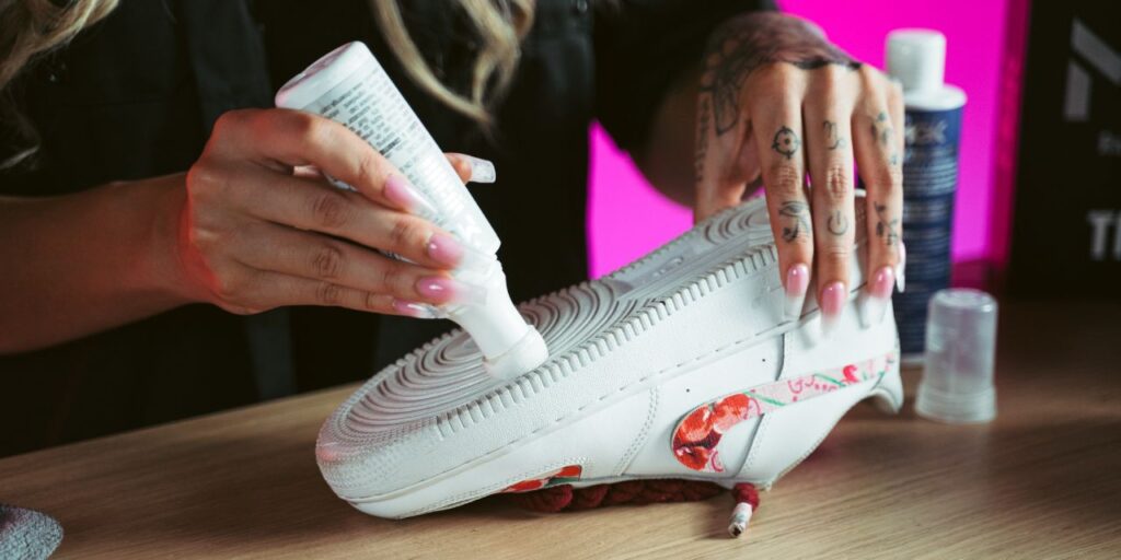 Woman applies Shoe MGK White Touch-up to the soles of white Nike shoes