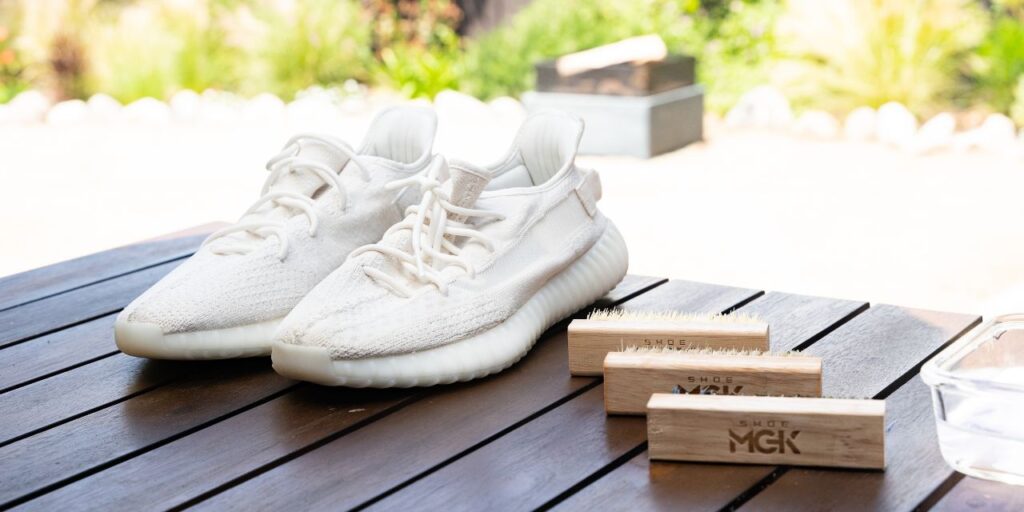 A pair of white Yeezys next to Shoe MGK Brushes