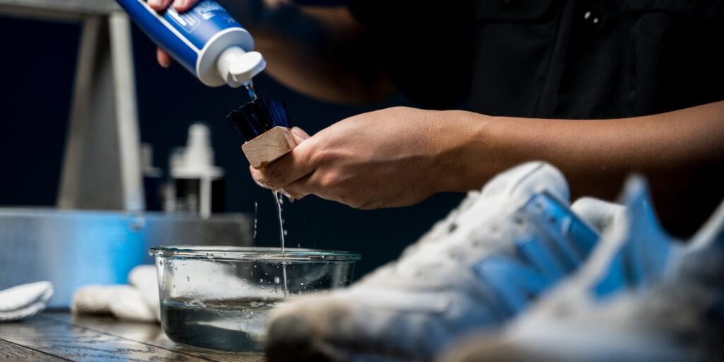 Man pours the Shoe MGK Cleaner and Conditioner next to the New Balance 574