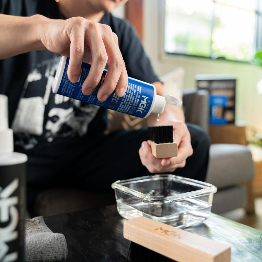 Man pours Shoe MGk Cleaner and Conditioner onto a shoe brush over a bowl of water