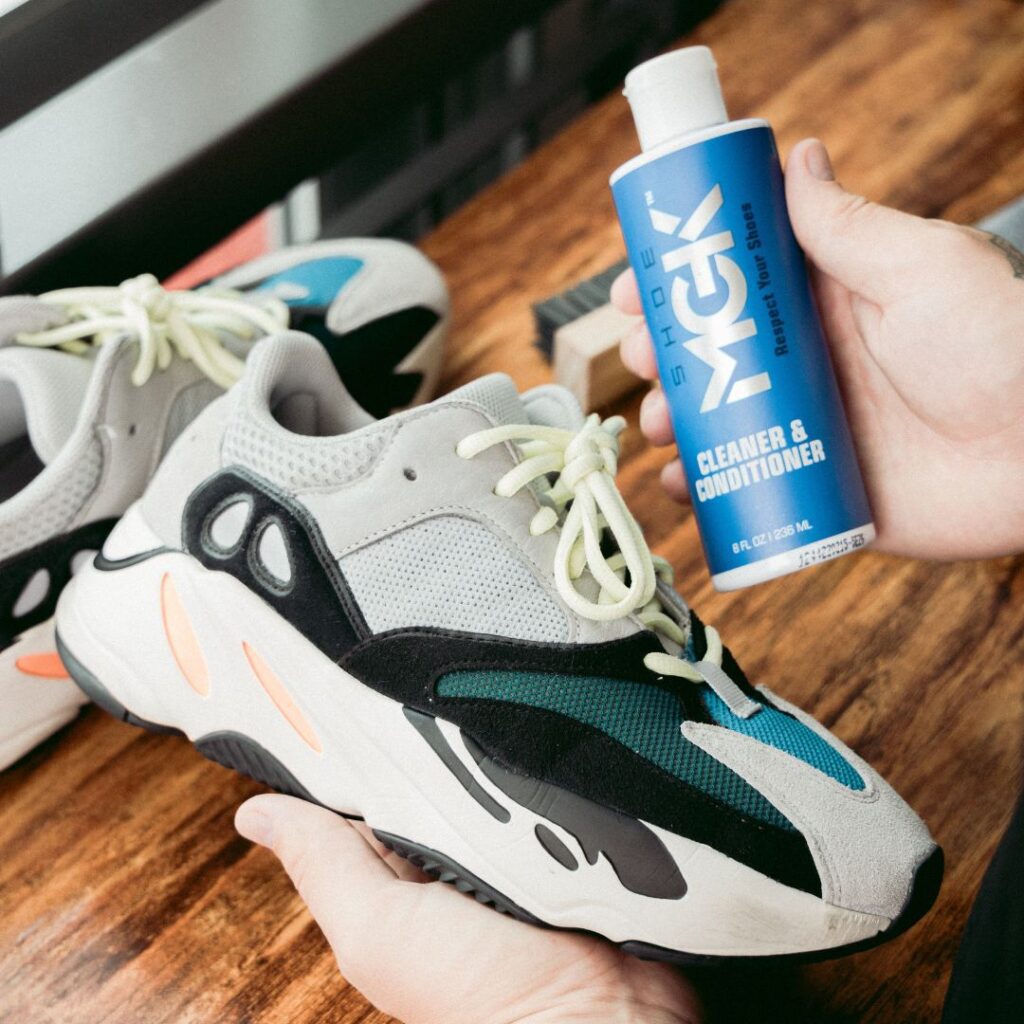 Man holds a bottle of the Shoe MGK Cleaner and Conditioner next to a pair of shoes