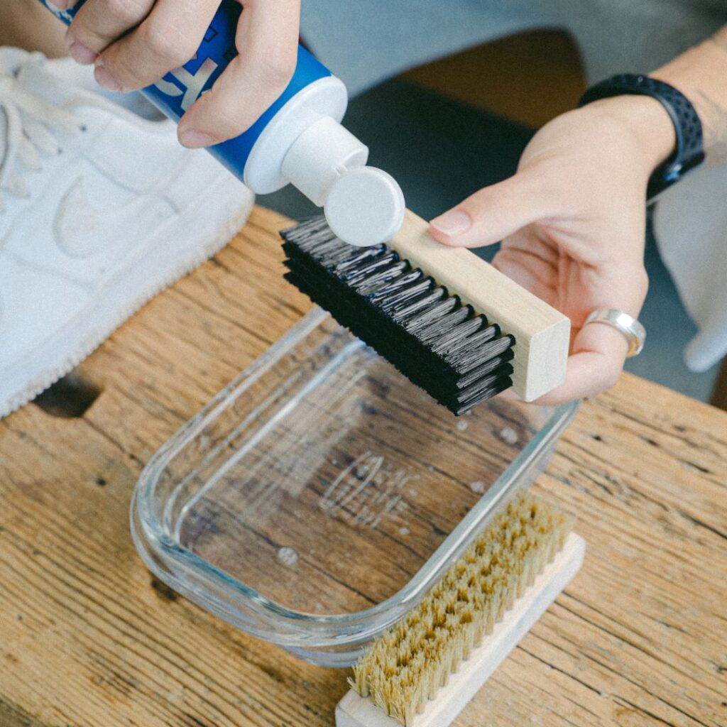 Man pours Shoe MGK Cleaner and Conditioner onto a shoe brush over a bowl of water