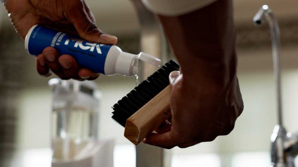 Man pours the Shoe MGK Cleaner and Conditioner onto a shoe brush