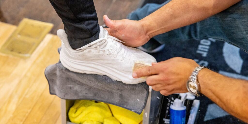 A man cleans a pair of white shoes with Shoe MGK